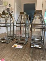 Four brass-framed clear glass lanterns on a wooden table, one missing handle.