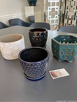 Set of four small flower pots on a grey surface with a white wall background, showing varied shapes and colors.