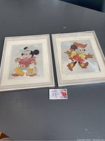 Two framed foil art pieces of Disney characters Mickey Mouse and Minnie Mouse in cowboy attire displayed on a table.