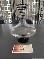 Full view of the clear glass wine decanter with black spiral design around the neck, on a table with a reflective surface.