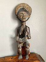 Front view of a carved wooden African statue of a seated figure with detailed facial features and patterns on the head.