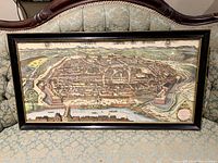 Full view of framed vintage map print of Vienna on a patterned fabric sofa.