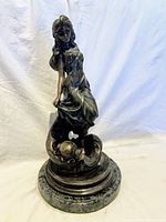 Full view of bronze statue of a woman standing on round pedestal.