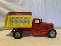 Side view of vintage Coca Cola metal toy truck with yellow rear cargo display holding six clear glass Coca Cola bottles.