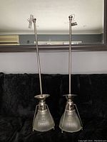 Pair of Union Lighting drop light fixtures standing upright on a couch, showing the ribbed glass shade and metal rods with top mounts.