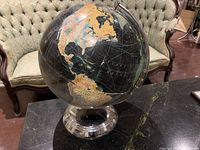 Globe showing the Americas, black water with gold and blue continents, sits on reflective silver base.