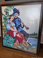 Full view of framed hand-embroidered artwork showing a couple in traditional Ukrainian clothes next to a river.