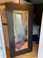 Full view of the large rectangular mirror with dark brown wood frame reflecting indoor and outdoor scenes.