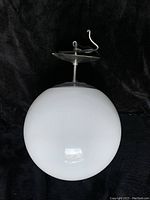 Ceiling light fixture with round white glass globe against black background showing the metal mounting plate and hanging rod with attached electrical wiring.