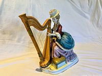 Porcelain musical lady figurine playing harp, view from front left side showing intricate details of dress, harp, and musical box.