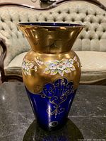 Overall view of blue and gold vase with floral design on table in front of tufted sofa