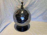 Closed view of the shiny metallic spherical cover with a pump on top, reflecting the surroundings