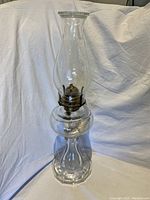 Full view of the vintage glass oil lamp showing the clear glass chimney, brass burner, and faceted base.