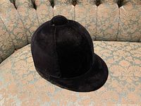 Black velvet vintage riding hat displayed on patterned sofa.