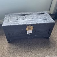 Front angle showing carved ships, floral border, brass lock plate, and carved feet of the wooden chest.