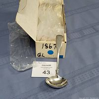 Rogers Bros 1867 pattern silverplate gravy ladles in a box, one ladle displayed standing showing bowl and handle details, plastic wrapping inside the box.
