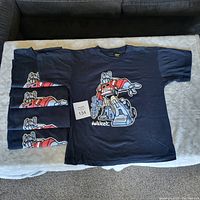 Five black youth large size Transformers Autobot T-shirts stacked with one shirt unfolded showing front graphic