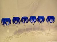 Front view of all six cobalt blue crystal wine glasses arranged in a row showing the color and cut design around the bowl.