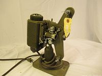 Full side view of antique film projector showing metal body, knob for film reel on arm, and power cord.