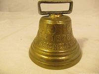 Close-up front and side views of the antique brass bell showing embossed details and patina.