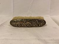 Back view of the antique sterling silver brush showing detailed embossed floral and nature design and natural bristles.