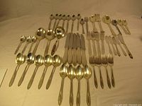Full assortment of vintage cutlery laid out including spoons, forks, and knives, all with silver tone and gold accents