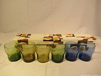 Six colored tumblers (two green, two amber, two blue) arranged in front of original patterned boxes