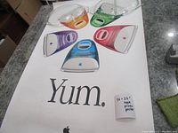 Photo showing the colorful translucent iMac images on the poster with the word 'Yum.' and a note indicating the size and description.