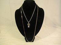 Front view of two silver necklaces displayed on black stand, one with pendant, one longer chain without pendant.