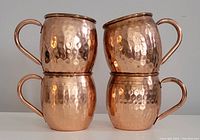 Front view of the four copper Moscow Mule mugs stacked in two pairs, showing hammered texture and handles.