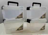 Four new translucent plastic storage bins arranged in two stacks of two, showing black handles and clips with branding labels.