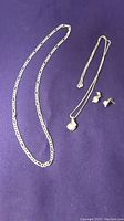 Two gold chains and pearl earrings on purple fabric