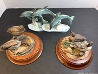 Photo showing all three figurines: ceramic dolphin sculpture and two sets of bird figurines on wooden plaques