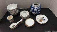 Overview of set including bowls, plates, spoons, cup, and blue vase arranged on table.