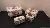 Full set displayed against black background showing 2 lidded boxes, lighter and 4 small plates, all hand painted with rose motifs and gold trim.