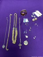 Full view of all jewelry items laid out on purple fabric background, showing necklaces, earrings, bracelet, brooch, and loose components.