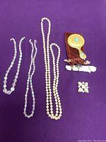 Photo showing two crystal bead necklaces, one long strand of faux pearls, small jewelry pouch with flower decoration, a brooch, and two small charm items