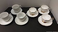 Photo showing six cups and saucers arranged against a white background, three with silver trim and three with gold trim