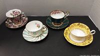 All four cups and saucers displayed together, showing varied floral and gold designs