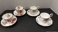 FourRoyal Albert tea cups and saucers with two distinct floral patterns displayed on a black surface
