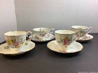 Four porcelain teacups and saucers with floral patterns and gold trim arranged in a row.