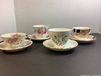 Front view of the four cups and saucers arranged in a row, showing their different floral patterns and designs.