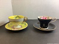 Two porcelain cups and saucers, one yellow with floral design, one black with floral interior design.