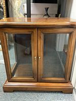 Front view of wooden display cabinet showing double glass doors with brass knobs.