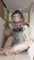 Lindsey doll by Mavis Sayder wrapped in plastic inside original box, dressed in striped overalls and engineer hat, holding toy train engine