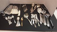 Showing mixed flatware pieces including forks, spoons, knives with Bakelite handles, ladles, and a sharpening steel.