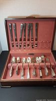 View of the open flatware box showing upper slot section with knives and lower section with various forks and spoons arranged in rows