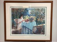 Full view of framed print showing a woman seated at a table with flowers and teapot in an outdoor garden setting.