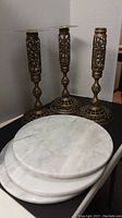 Photo showing three ornate brass stands with intricate lattice design and three round white marble tabletops stacked in front