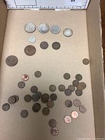 Photo showing a wide assortment of vintage Canadian coins scattered on a cardboard surface including large dollar coins and various smaller pennies.